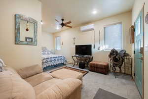 Living room featuring an AC wall unit, ceiling fan, and light carpet