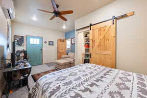 Bedroom with a wall mounted air conditioner, a textured ceiling, ceiling fan, a barn door, and carpet floors