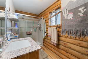 Bathroom with wood-type flooring, vanity, rustic walls, and an enclosed shower