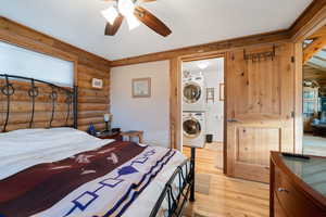 Bedroom with light hardwood / wood-style flooring, ceiling fan, log walls, multiple windows, and stacked washer / dryer