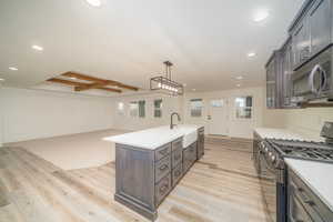 Kitchen featuring stainless steel appliances, light hardwood / wood-style flooring, beamed ceiling, pendant lighting, and a kitchen island with sink