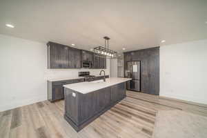 Kitchen featuring light hardwood / wood-style floors, dark brown cabinetry, pendant lighting, and appliances with stainless steel finishes