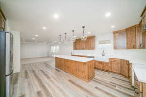 Kitchen featuring sink, hanging light fixtures, stainless steel fridge with ice dispenser, a kitchen island, and light wood-type flooring