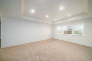 Empty room with a raised ceiling, light colored carpet, and wooden ceiling