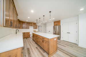 Kitchen featuring sink, a center island, stainless steel refrigerator with ice dispenser, pendant lighting, and light wood-type flooring