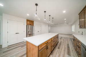 Kitchen with decorative light fixtures, a kitchen island, stainless steel appliances, and light hardwood / wood-style flooring