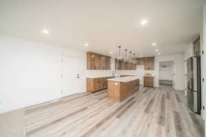 Kitchen featuring stainless steel fridge, sink, decorative light fixtures, light hardwood / wood-style floors, and a kitchen island