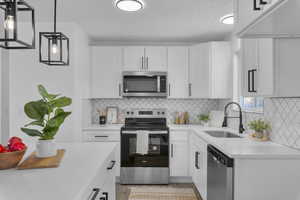 Kitchen featuring sink, white cabinetry, stainless steel appliances, and hanging light fixtures