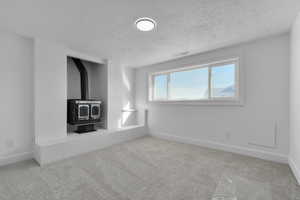 Unfurnished living room featuring a textured ceiling, light colored carpet, and a wood stove