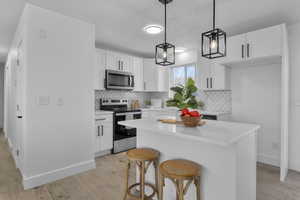 Kitchen featuring white cabinetry, hanging light fixtures, appliances with stainless steel finishes, and light hardwood / wood-style flooring