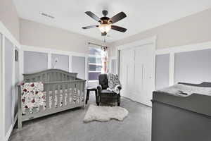 Carpeted bedroom featuring ceiling fan, a closet, and a nursery area