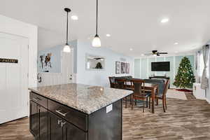 Kitchen with a center island, wood-type flooring, hanging light fixtures, ceiling fan, and dark brown cabinetry