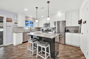 Kitchen with a center island, light hardwood / wood-style flooring, appliances with stainless steel finishes, tasteful backsplash, and white cabinetry