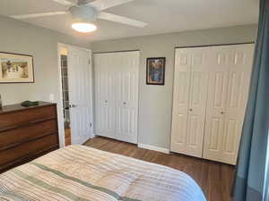 Bedroom with ceiling fan, dark wood-type flooring, and two closets