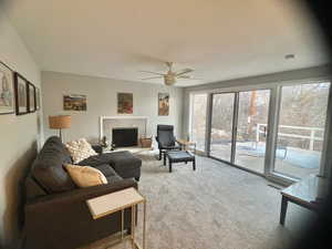 Living room featuring carpet flooring, a tile fireplace, ceiling fan, and a healthy amount of sunlight