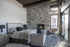 Bedroom with beam ceiling, wooden ceiling, a high ceiling, a stone fireplace, and access to outside