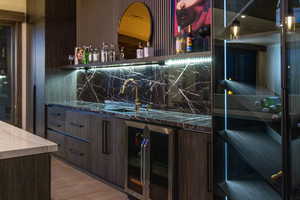 Bar with sink, tasteful backsplash, wine cooler, light hardwood / wood-style floors, and dark brown cabinets