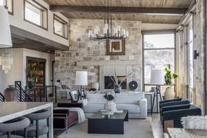 Living room featuring beamed ceiling, a stone fireplace, wood ceiling, and a chandelier