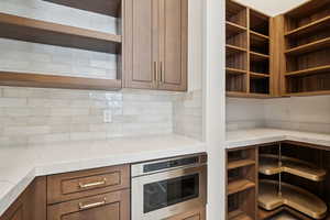 Kitchen featuring light stone counters, stainless steel oven, backsplash, and open shelves