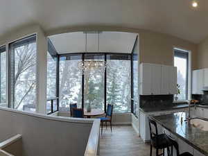 Kitchen with backsplash, dark stone counters, white cabinets, sink, and light hardwood / wood-style floors