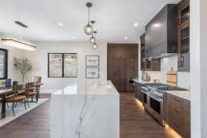 Kitchen featuring sink, wall chimney range hood, dark hardwood / wood-style flooring, range with two ovens, and a kitchen island with sink