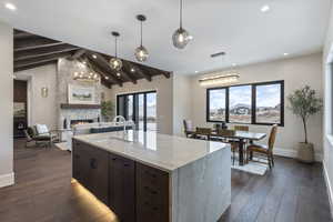 Kitchen featuring sink, vaulted ceiling with beams, a fireplace, an island with sink, and dark hardwood / wood-style flooring