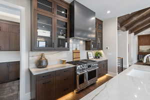 Kitchen with range with two ovens, wall chimney exhaust hood, dark hardwood / wood-style floors, beam ceiling, and light stone counters