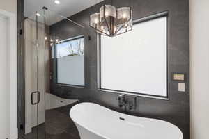 Bathroom with shower with separate bathtub, tile walls, and an inviting chandelier