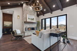 Living room with beam ceiling, high vaulted ceiling, a chandelier, dark hardwood / wood-style floors, and a stone fireplace