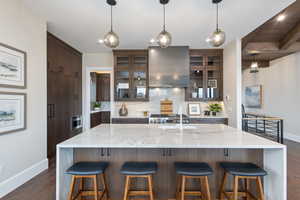 Kitchen with a kitchen bar, dark hardwood / wood-style flooring, a spacious island, sink, and wall chimney range hood