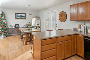 Kitchen featuring kitchen peninsula, light wood-type flooring, hanging light fixtures, and dishwasher