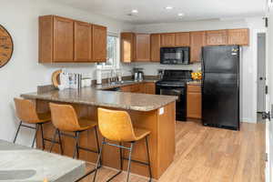 Kitchen featuring kitchen peninsula, light wood-type flooring, a breakfast bar, sink, and black appliances