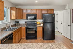 Kitchen with black appliances, light hardwood / wood-style floors, and sink