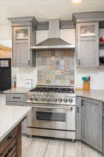 Kitchen featuring backsplash, high end range, wall chimney range hood, and light wood-type flooring