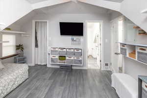 Bedroom with ensuite bath, dark hardwood / wood-style flooring, and lofted ceiling