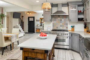 Kitchen featuring decorative backsplash, wall chimney range hood, decorative light fixtures, an inviting chandelier, and stainless steel stove