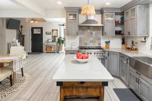 Kitchen with wall chimney exhaust hood, hanging light fixtures, light hardwood / wood-style flooring, a notable chandelier, and high end range