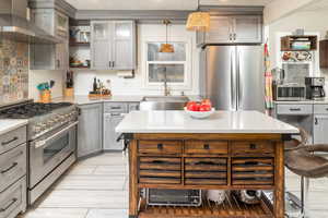 Kitchen with sink, wall chimney exhaust hood, pendant lighting, decorative backsplash, and appliances with stainless steel finishes