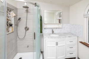 Bathroom featuring vanity, decorative backsplash, and a shower with door