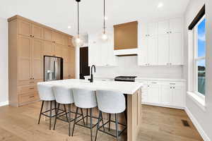 Kitchen featuring white cabinets, stainless steel appliances, a wealth of natural light, and an island with sink