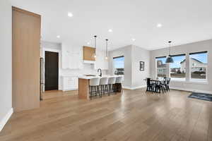 Kitchen featuring light wood-type flooring, a breakfast bar, pendant lighting, white cabinetry, and an island with sink