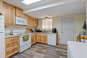 Kitchen featuring light brown cabinetry, white appliances, light hardwood / wood-style floors, and sink