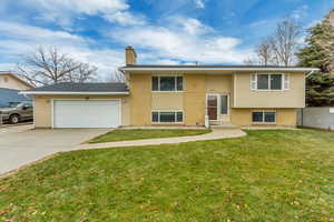 Raised ranch featuring a garage and a front lawn