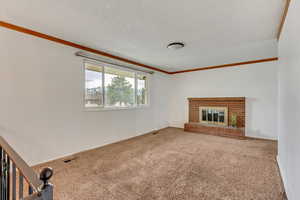 Unfurnished living room featuring ornamental molding, carpet floors, a textured ceiling, and a brick fireplace