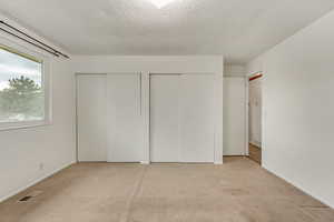 Unfurnished bedroom featuring multiple closets, light carpet, and a textured ceiling