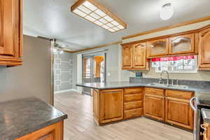 Kitchen with ceiling fan, crown molding, sink, light hardwood / wood-style flooring, and stainless steel stove