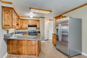 Kitchen with kitchen peninsula, appliances with stainless steel finishes, ornamental molding, sink, and light hardwood / wood-style flooring