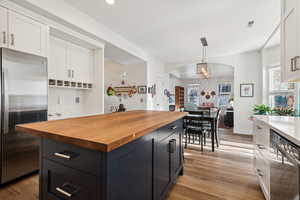 Kitchen featuring a center island, stainless steel fridge, light wood-type flooring, butcher block countertops, and decorative light fixtures