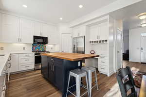 Kitchen with dark wood-type flooring, butcher block countertops, a kitchen island, white cabinetry, and stainless steel appliances