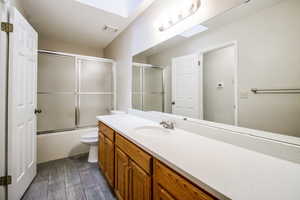 Full bathroom featuring a skylight, vanity, hardwood / wood-style flooring, enclosed tub / shower combo, and toilet